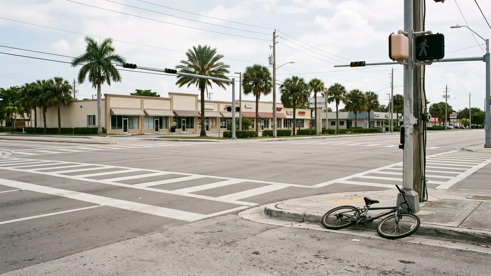 Un cruce peatonal en una avenida ancha de Hialeah con una bicicleta caída junto a la acera